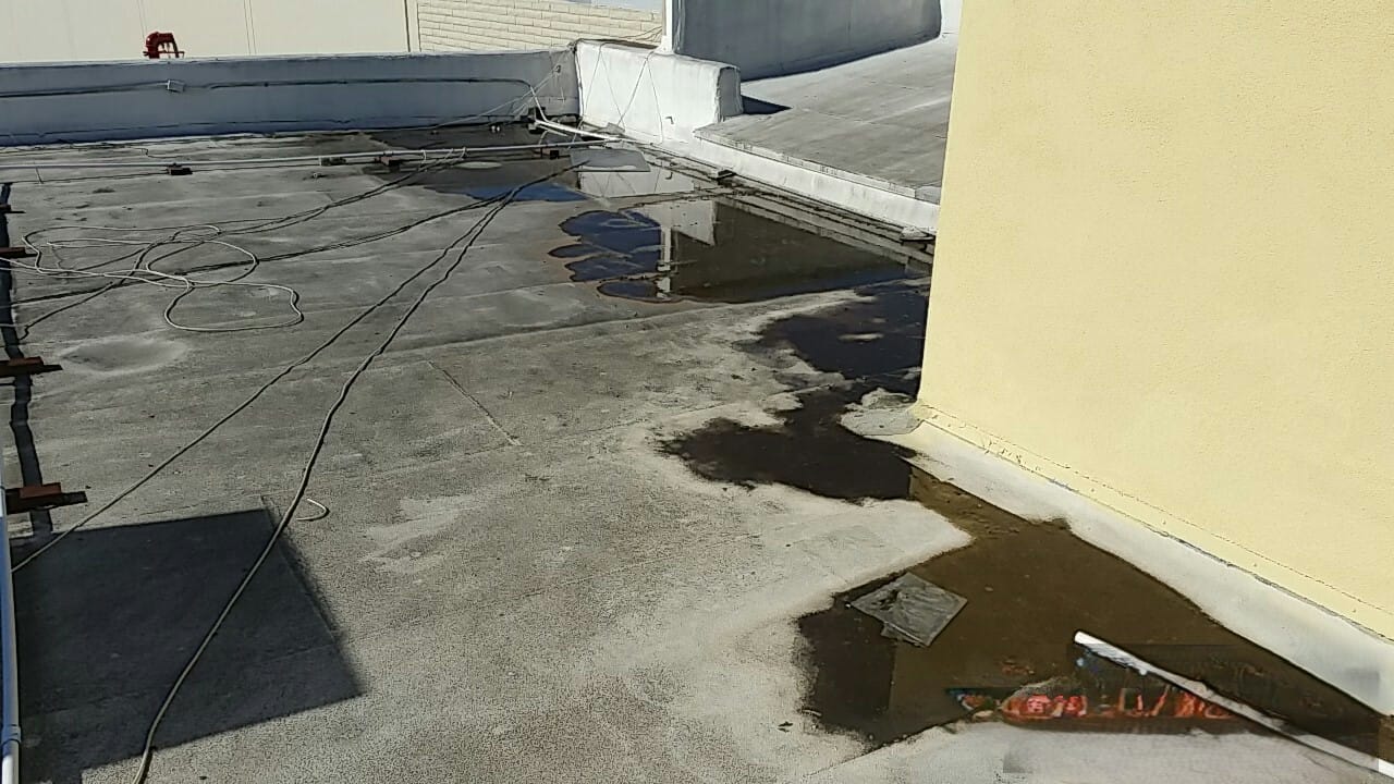 Flat commercial rooftop with standing water pooling near a yellow wall and loose cables on the surface