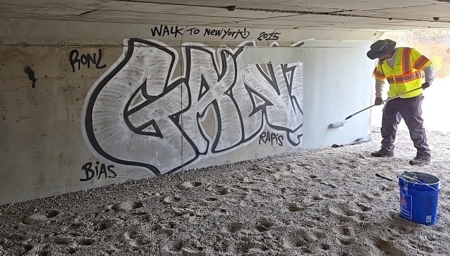 Graffiti being removed from a commercial exterior wall, with the cleaned area contrasting against the remaining tagging